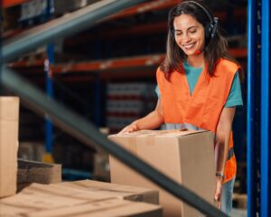 Warehouse worker wearing headset lifting cardboard box
